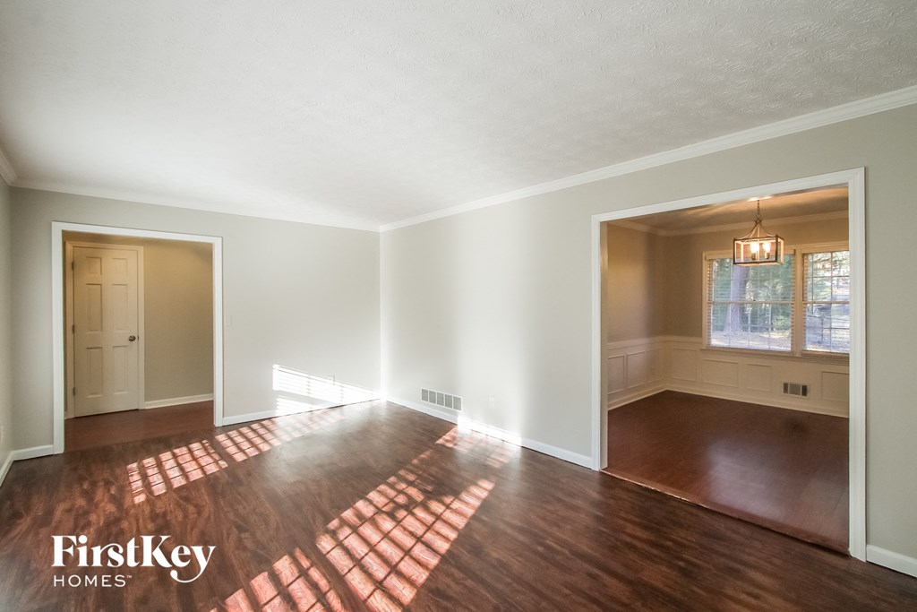 A room with wooden floors and white walls, with a window and a door visible.