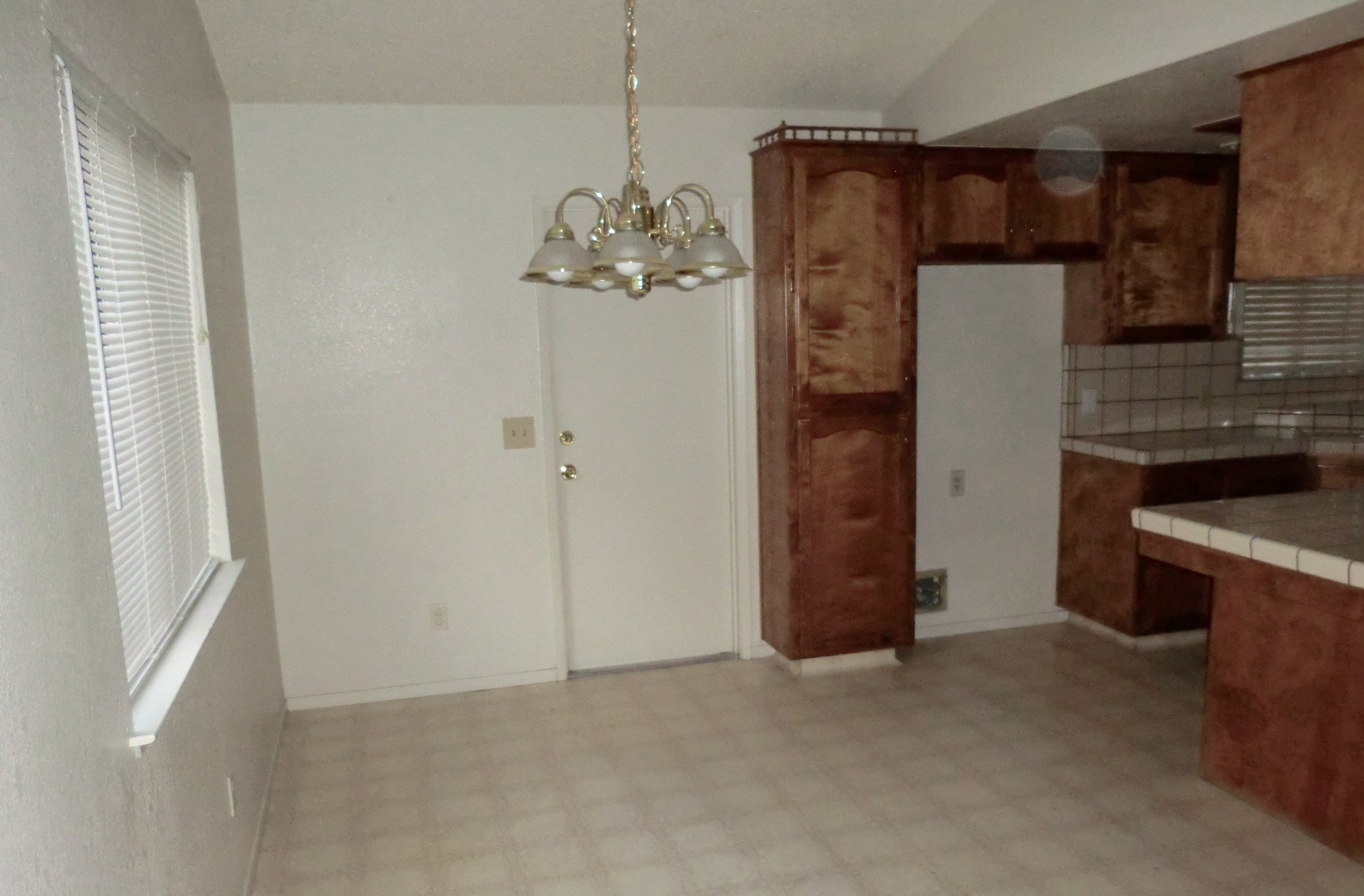 an empty living room with a kitchen and a chandelier