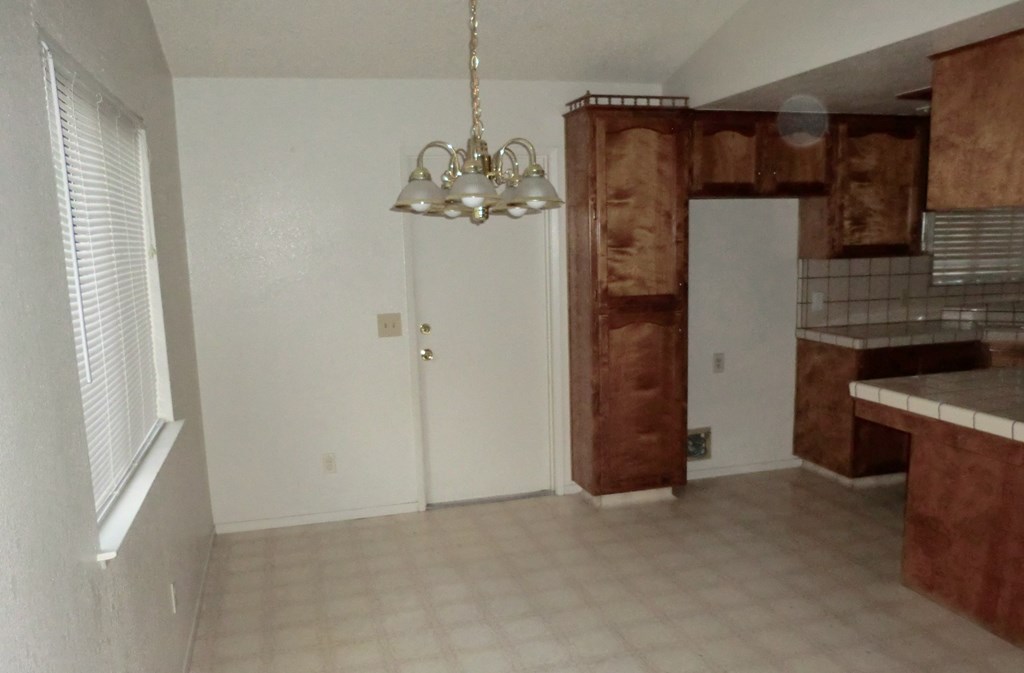 an empty living room with a kitchen and a chandelier
