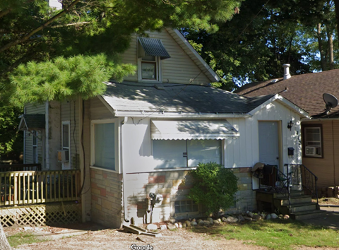 A white house with a brown roof and a porch.