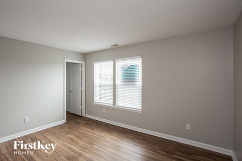 a bedroom with white walls and wood floors and a window