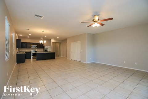 A spacious room with a ceiling fan and a kitchen area in the background.