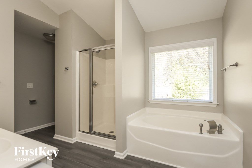 A white bathtub with a window above it in a bathroom.