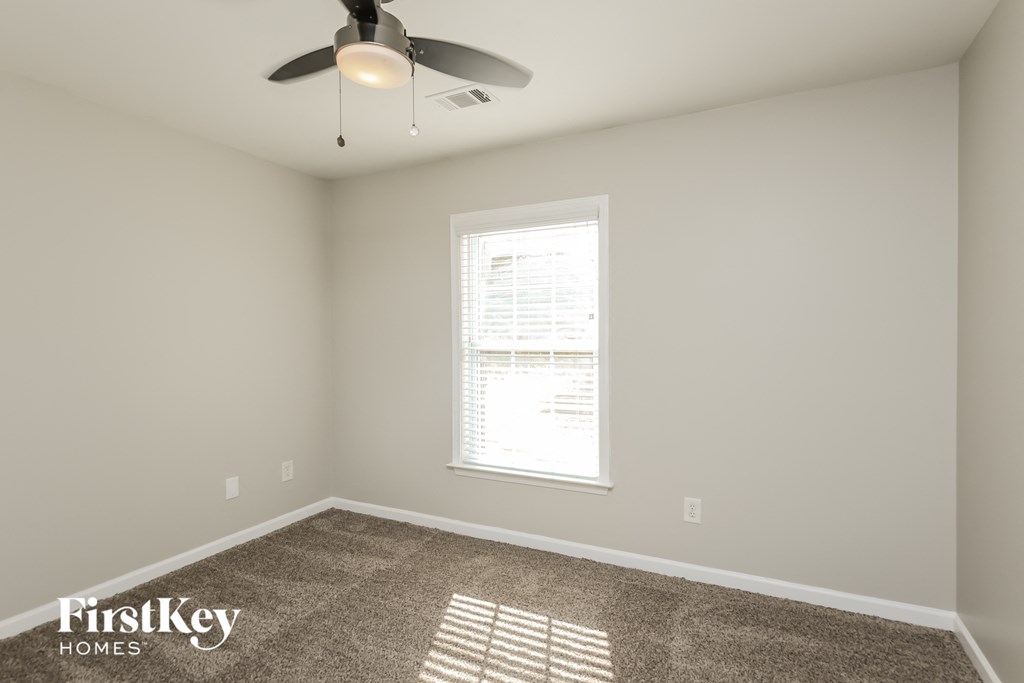 A room with a fan, carpet, and a window.