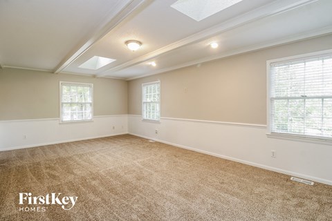 A spacious room with beige carpeting and two windows.