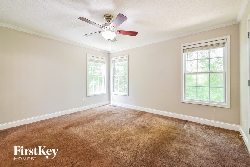 a carpeted living room with a ceiling fan and two windows
