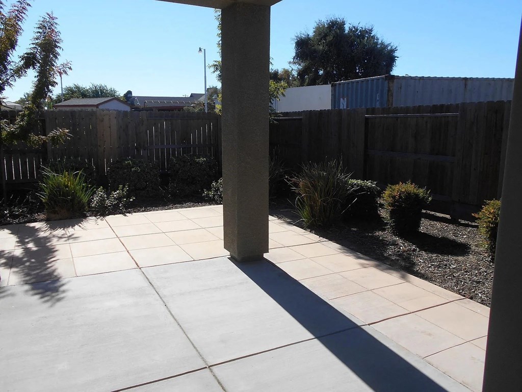 the side yard of a house with a concrete patio and a wooden fence