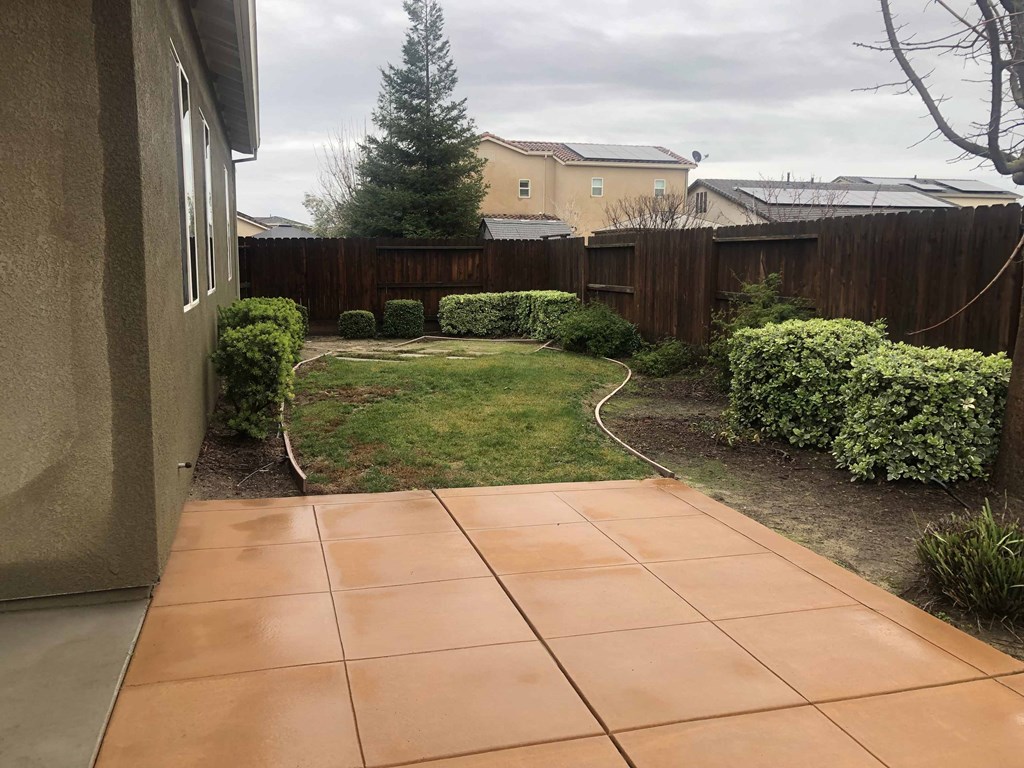 a backyard with a tiled patio and a yard with grass and a fence