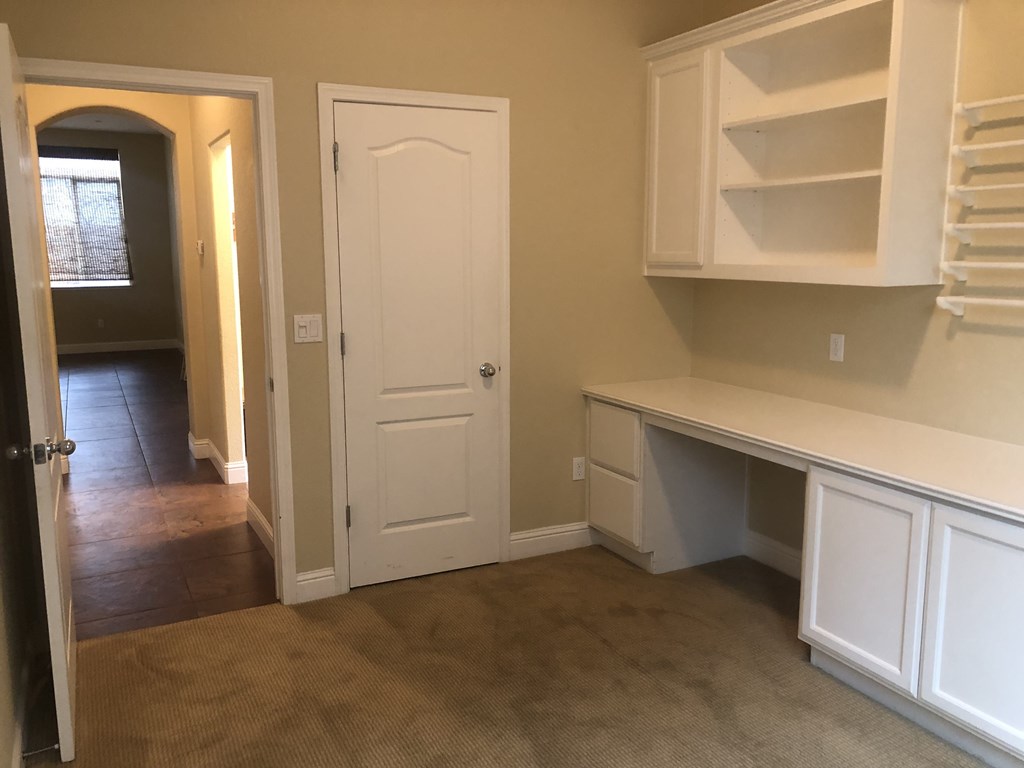 an empty room with white cabinets and a door into a hallway