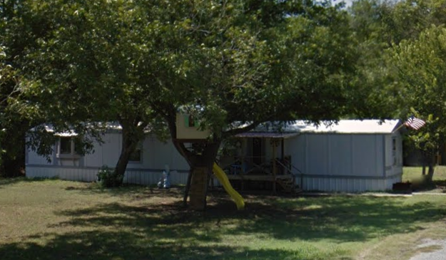 A tree in a yard with a white house in the background.