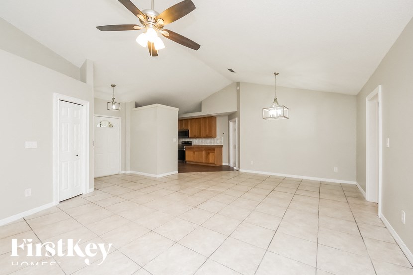 an empty living room with a ceiling fan and a kitchen