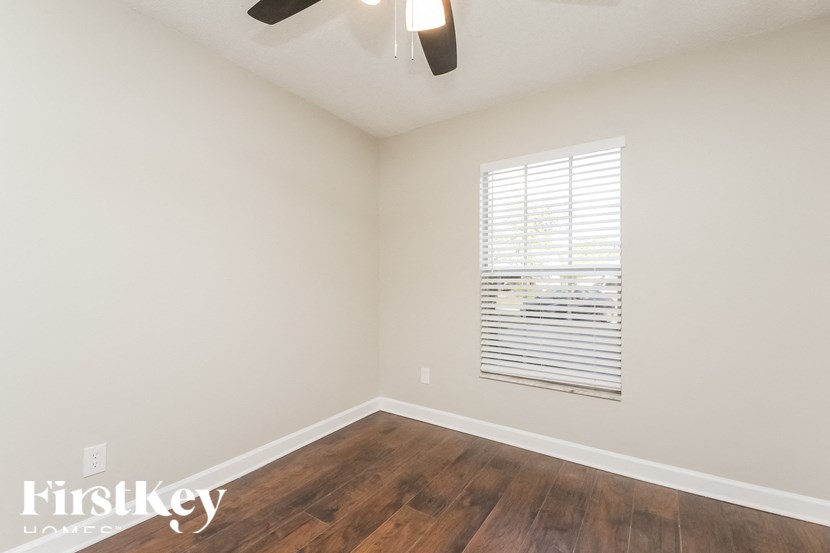 a bedroom with wood flooring and a window and a ceiling fan