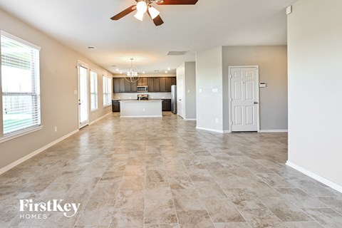 A spacious living room with a kitchen in the background and a fan on the ceiling.