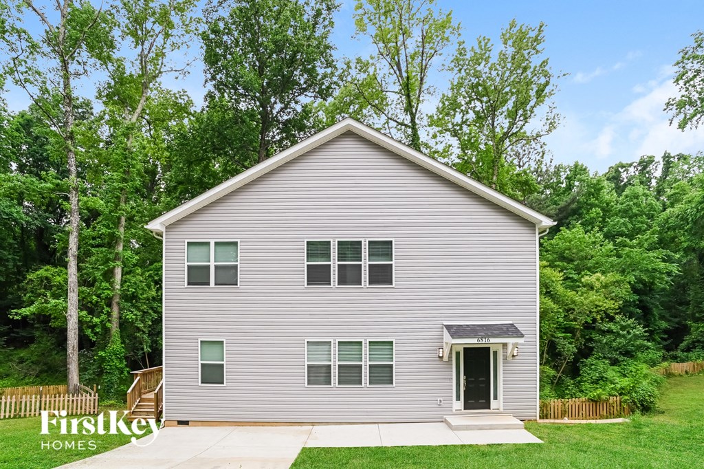 A house with a grey siding and a black door is surrounded by greenery.