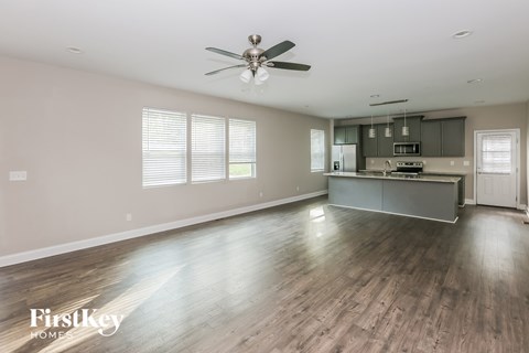 A spacious room with a ceiling fan and a kitchen area in the background.