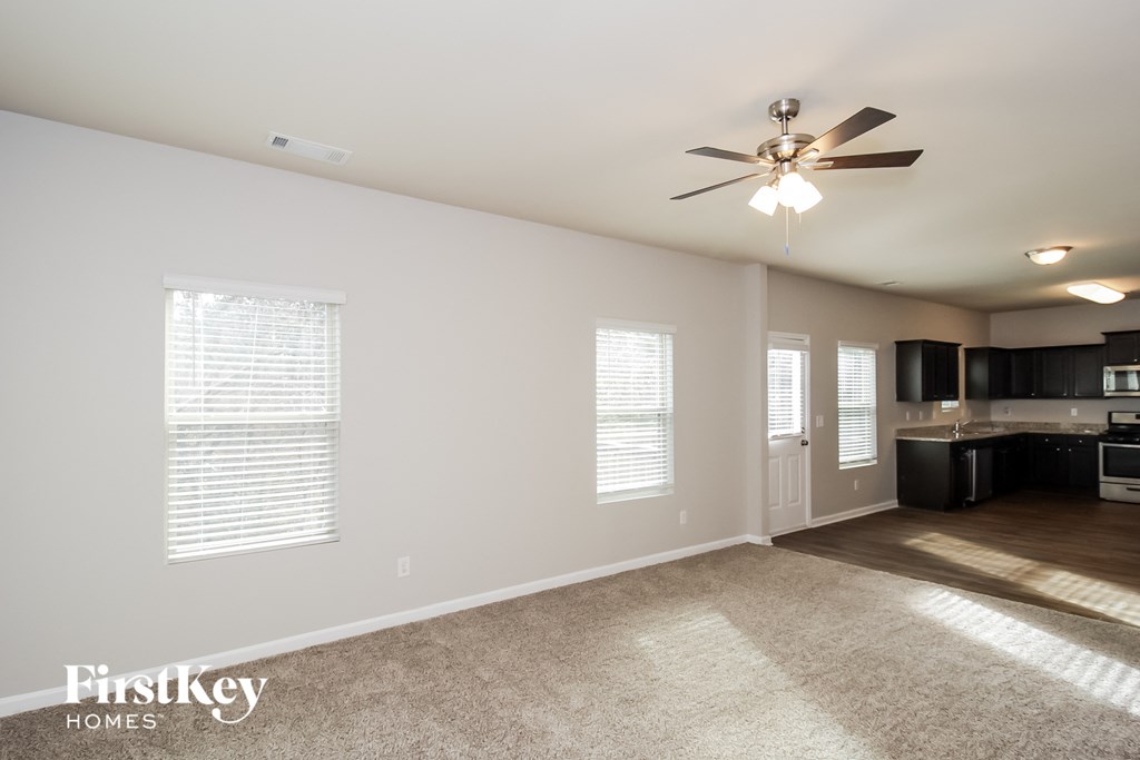 an empty living room with a ceiling fan and a kitchen