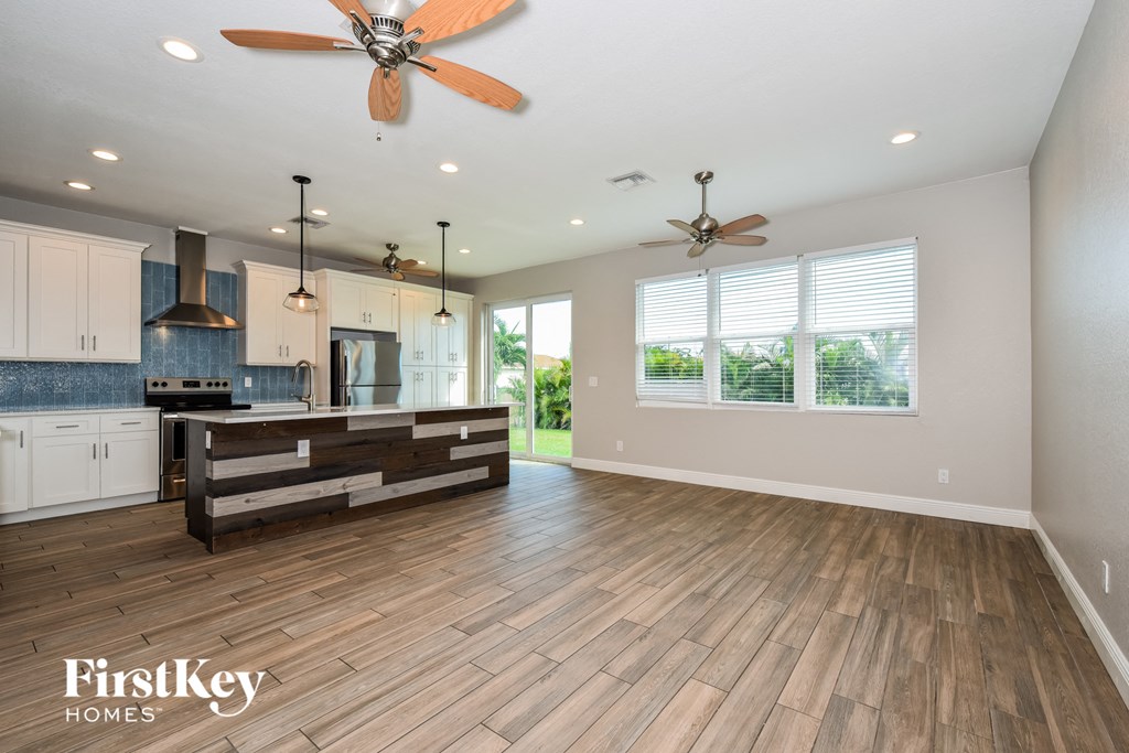 A spacious kitchen and living room with wooden floors and a ceiling fan.