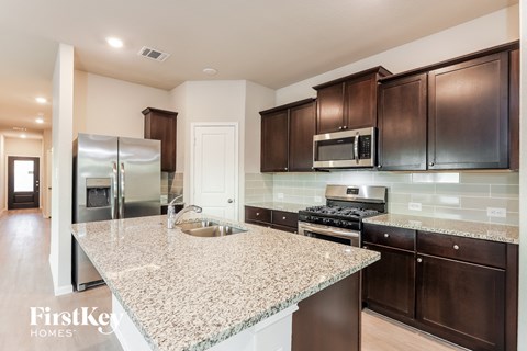 A kitchen with granite countertops and dark brown cabinets.