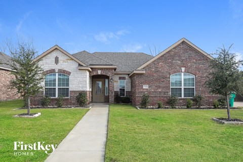 the front of a brick house with green grass and a sidewalk