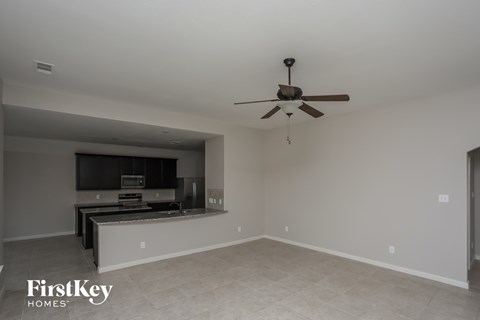 a empty living room with a ceiling fan and a kitchen