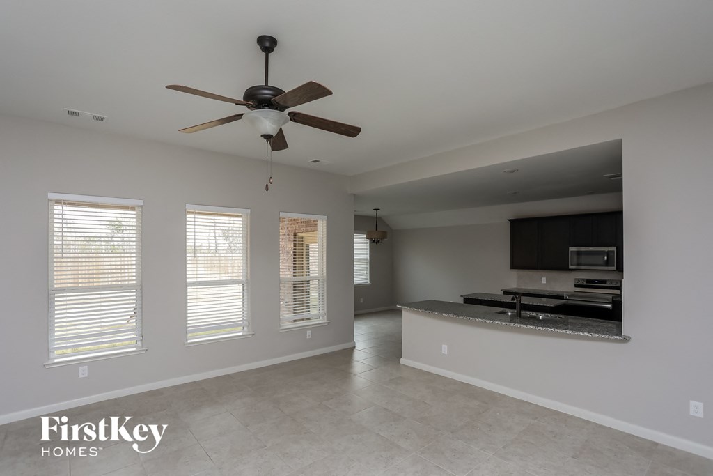 an empty living room with a ceiling fan and a kitchen