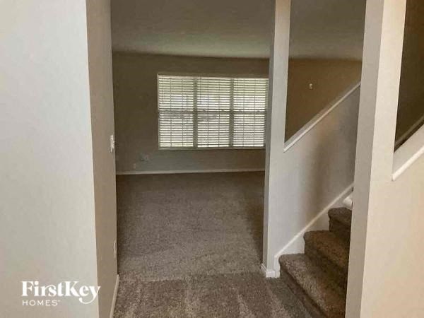 A hallway with a staircase and a window with blinds.
