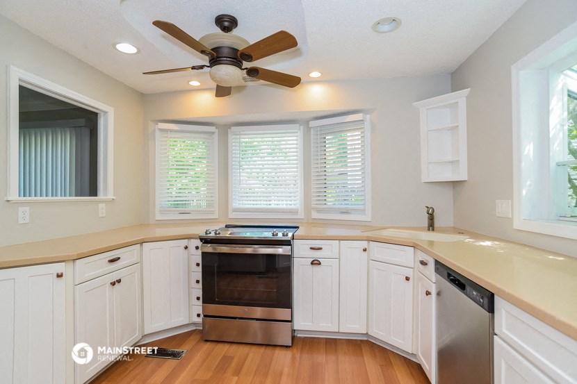 a kitchen with white cabinets and a stove and a ceiling fan