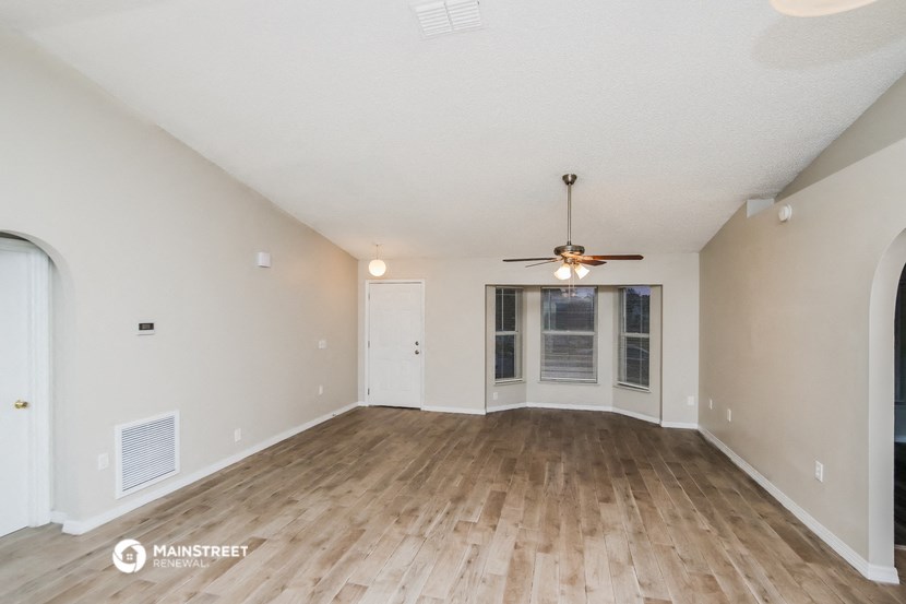 the spacious living room with hardwood flooring and a ceiling fan