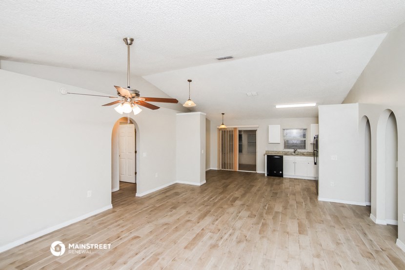 an empty living room with a ceiling fan and a kitchen