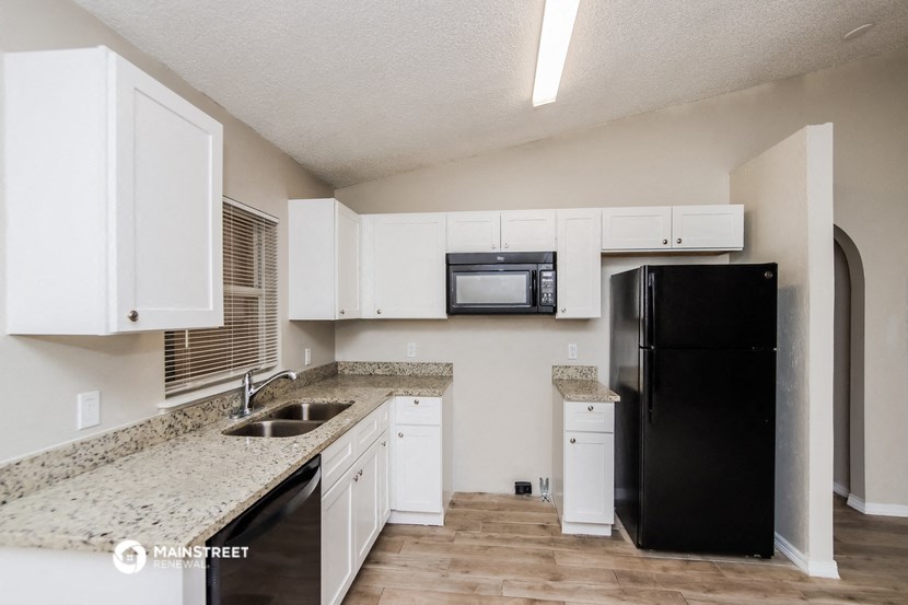 a kitchen with white cabinets and granite counter tops and a black refrigerator