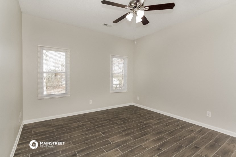 the spacious living room with wood flooring and a ceiling fan