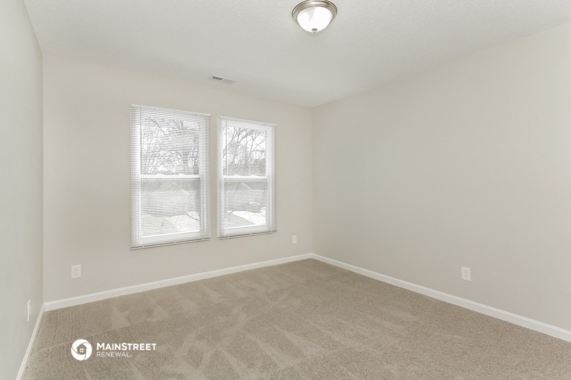 the spacious living room with two windows and carpeting