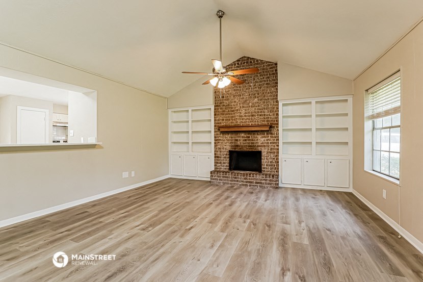 an empty living room with a brick fireplace and wooden floors
