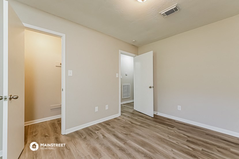 the spacious living room with wood flooring and a door to the bedroom