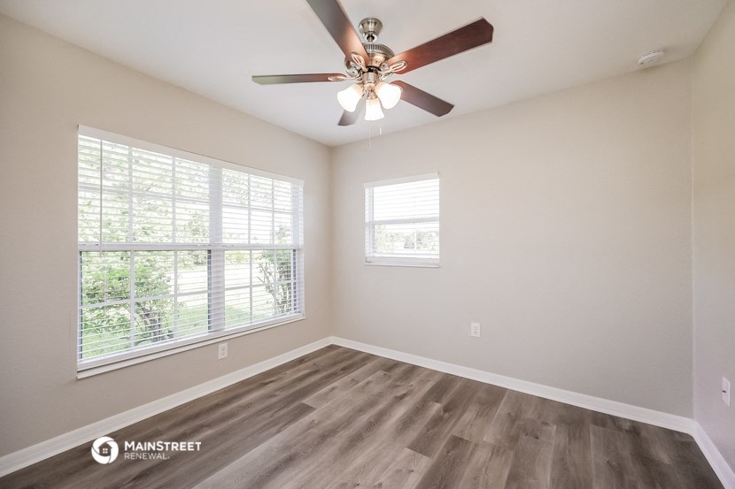 an empty living room with a ceiling fan and two windows