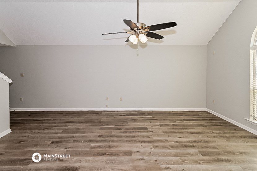 the spacious living room with wood flooring and a ceiling fan