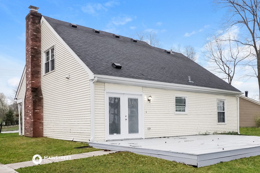 the back of a white house with a porch and a black roof