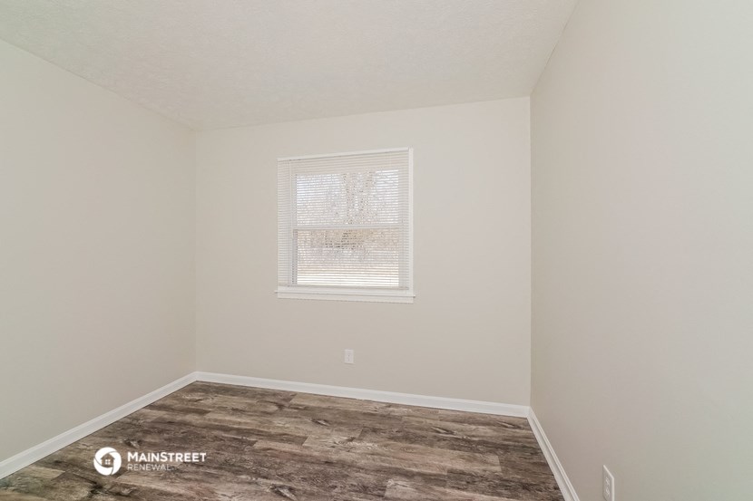 a bedroom with a wood floor and white walls and a window