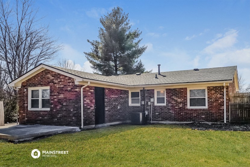 a brick house with a grassy yard and a tree in the background