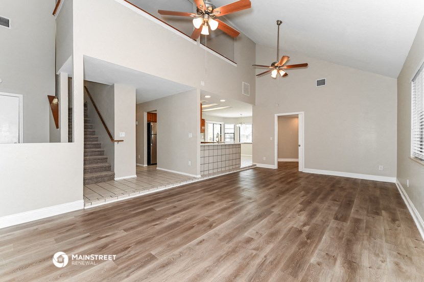 the living room and dining room of an empty house with two ceiling fans