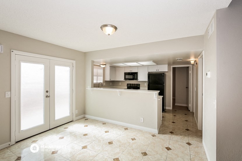 an empty living room with a kitchen and a door to a hallway