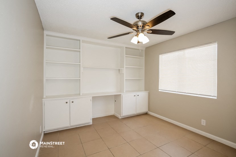 the spacious living room with built in shelves and a ceiling fan