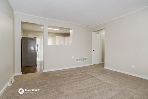 the spacious living room of an apartment with white walls and carpet