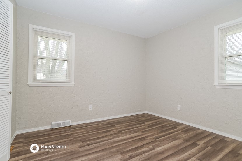 the interior of a room with wood flooring and two windows