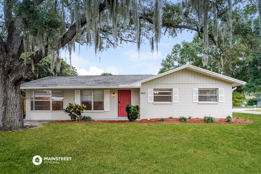 a small white house with a red door and moss covered tree