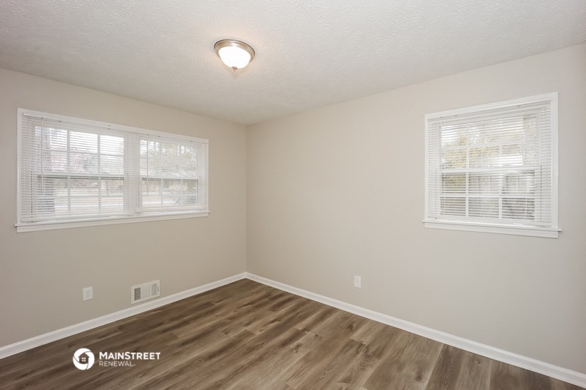 the interior of a bedroom with wood flooring and two windows