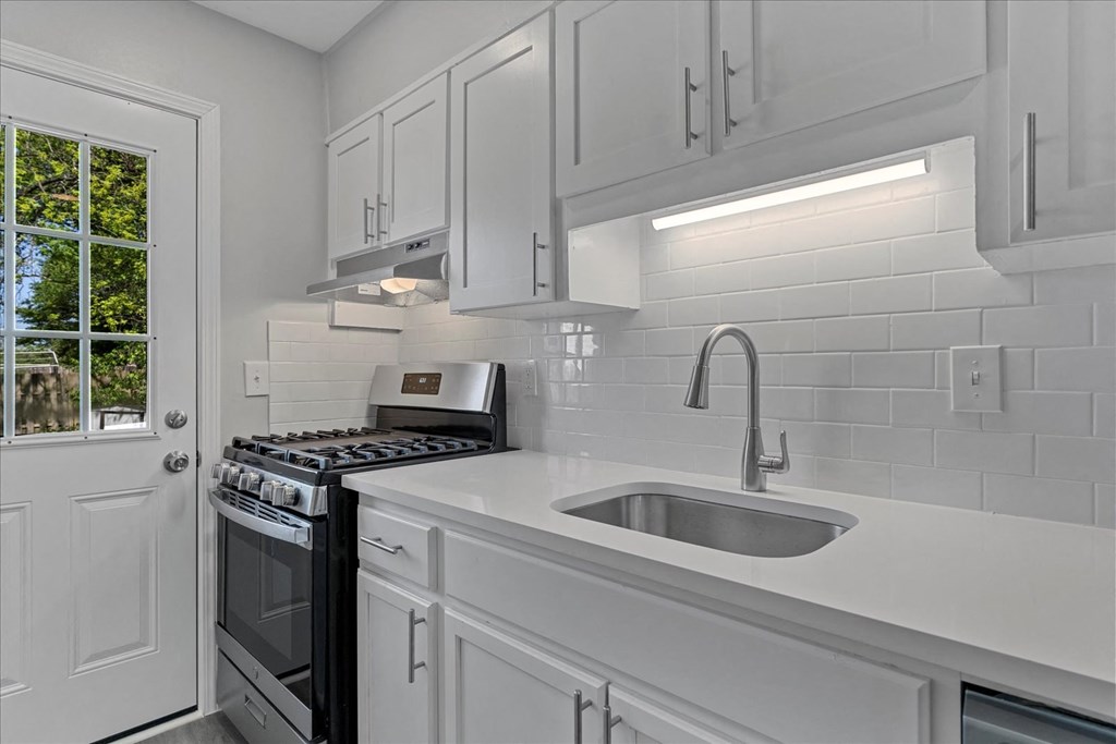 A white kitchen with a stove, sink, and cabinets.