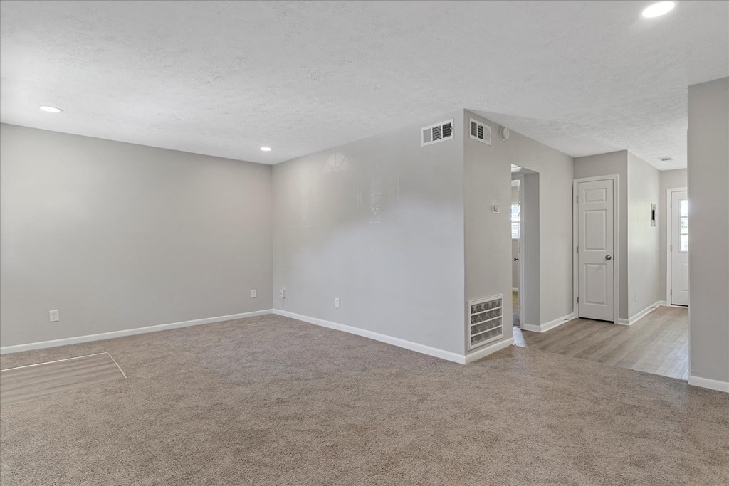 A spacious room with beige carpeting and white walls.
