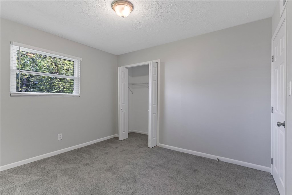 A room with a window, carpeted floor, and a door.
