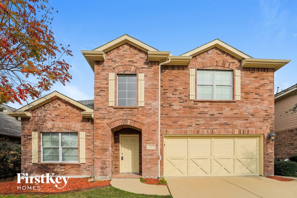 A brick house with a garage door and a tree with red leaves.